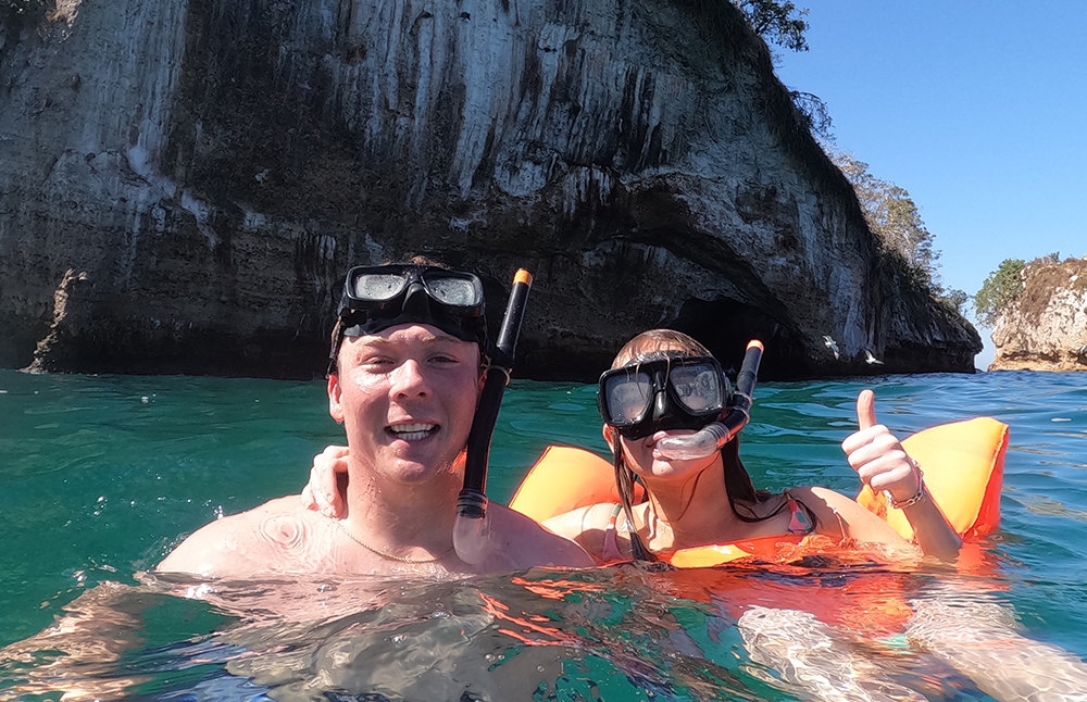 Dos personas buceando en aguas cristalinas, explorando el mundo submarino rodeados de peces y corales en un entorno tropical.