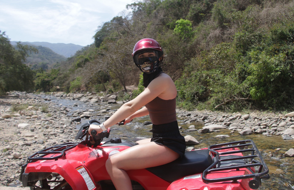 Mujer conduciendo una ATV sobre un camino de tierra rodeado de naturaleza, disfrutando de una experiencia aventurera al aire libre.