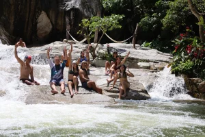 During a refreshing break from their tour, a group of people on a family tour sits by the river, raising their arms and enjoying nature.