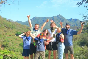 A group of people who did RZR routes poses happily in front of a mountainous landscape, raising their arms in victory.