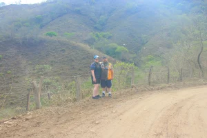Two people who joined a RZR route stop by a dirt road to take a photo with the hills in the background.