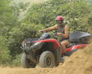 A man rides an ATV along a dirt path surrounded by vegetation as part of the extreme activities on the route.