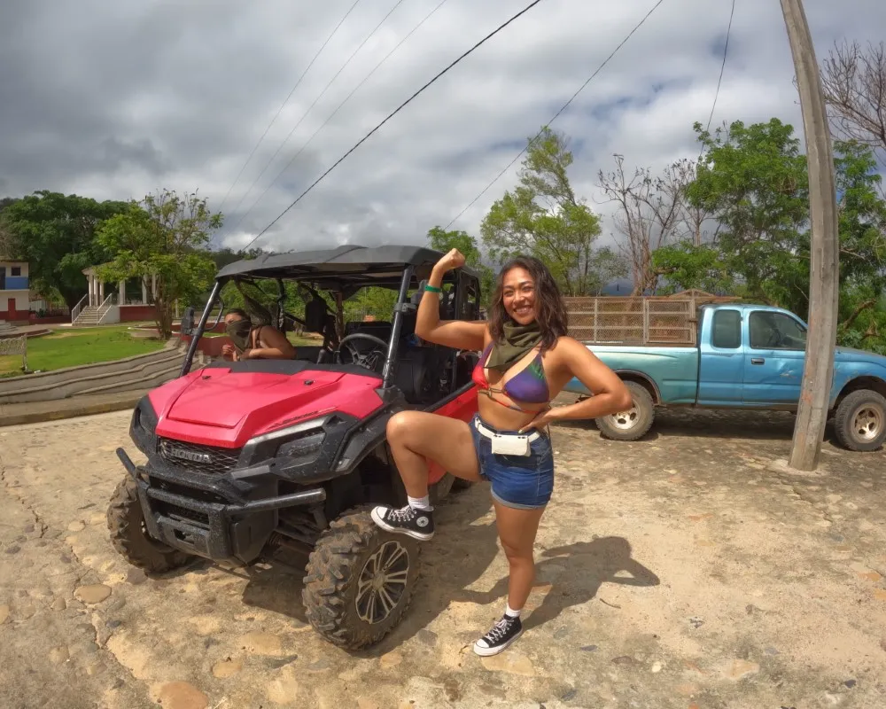 A smiling woman poses in front of an off-road vehicle, ready to start her rzr adventure in a rural setting.