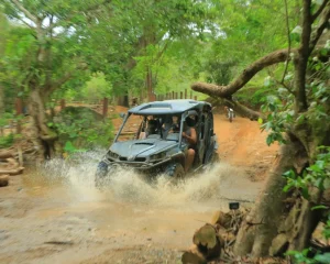 A RZR moves through mud and water while crossing a wooded area, part of an intense rzr adventure route.