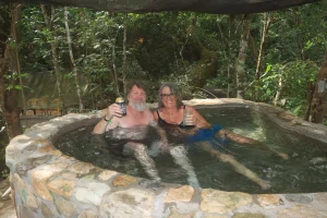 A couple relaxes in a thermal water pool in the middle of the forest, toasting during their Hot springs tour.
