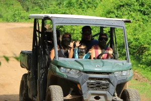 A group of people enjoys the Off road ATV tour together, smiling and waving as they ride through the forest in a shared ATV.
