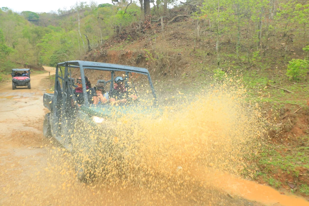 A group rides through the trails while the vehicle splashes water and mud, showing the thrill of Puerto Vallarta RZR Tours.