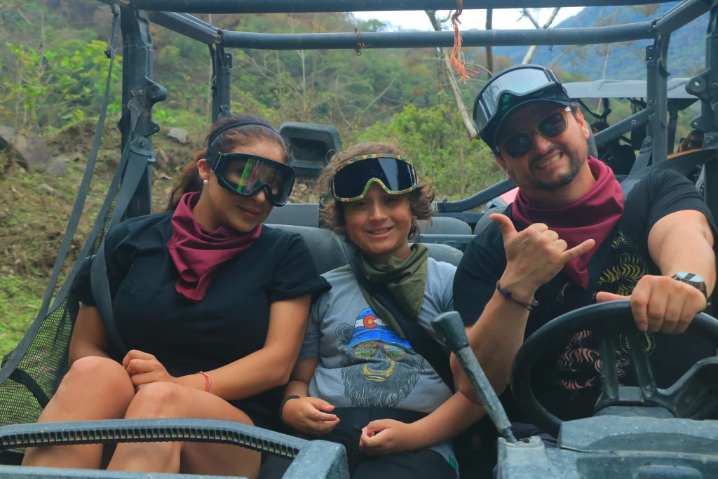 A happy child sits between two adults on an ATV ride through the jungle, one of the most exciting things to do in Puerto Vallarta with kids.
