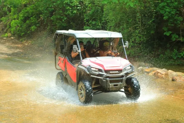 A red RZR moves through a muddy path, splashing water as part of the thrilling experience of ATV and RZR Adventures.