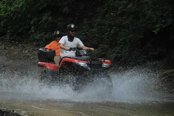 Driving a RZR through a stream, splashing water while exploring the tropical jungle.