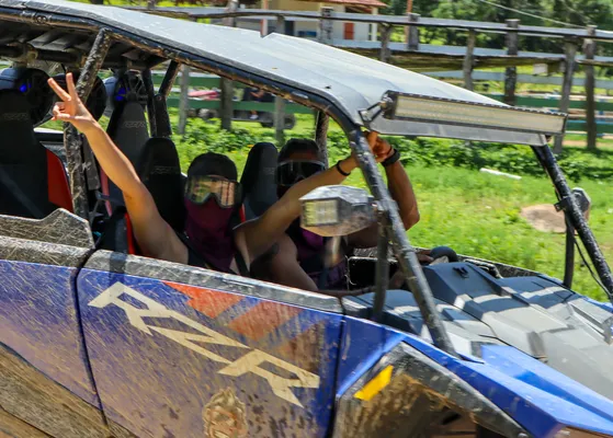 Two people raise their hands while riding a UTV, enjoying the thrill of the journey under the sun.
