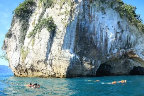A White Cliff Rises Above The Turquoise Sea, Creating An Ideal Setting For Practicing Snorkeling Among Rock Formations And Natural Shaded Areas.