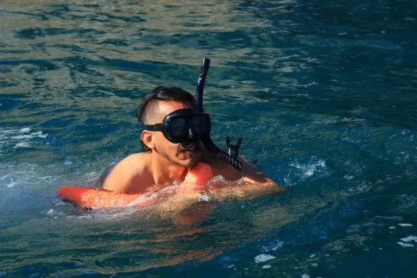 A person moves across the surface of the sea while holding their mask, ready to continue the snorkeling experience in calm, transparent waters.